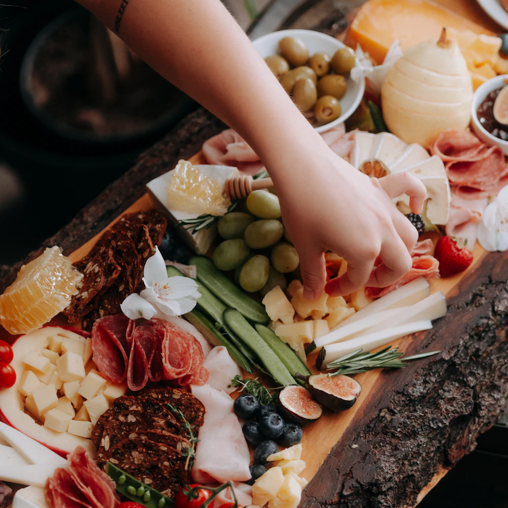 A hand reaching for prosciutto on an abundant rustic charcuterie board