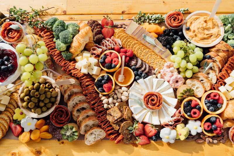 Overhead view of a large board of cheeses, salami roses, berries, crackers and dips