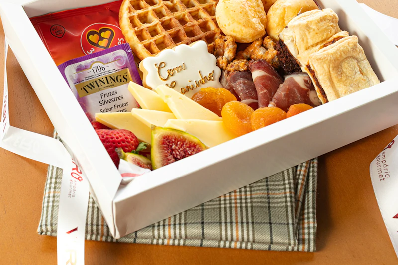 An open white gift box packed with cheese, fruit, waffles and snacks