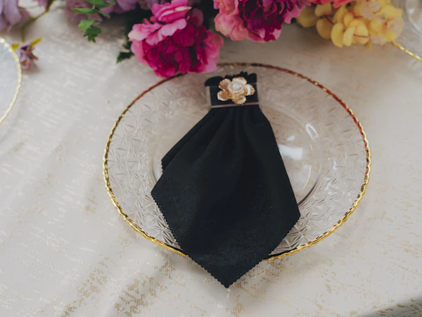 Clear glass plate with a gold rim and a folded black napkin